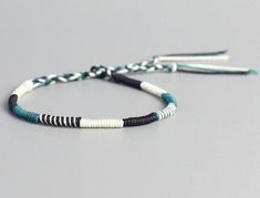 a white and blue bracelet with black beads on a gray background, one bead has two tassels