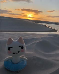 a toy cat sitting in the snow with a sunset in the back ground behind it