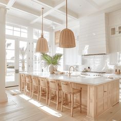 a large kitchen with white walls and wooden flooring, two pendant lights hanging over the island