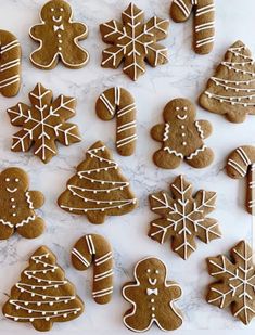 ginger cookies decorated with white icing on a marble counter top, including christmas trees and snowflakes