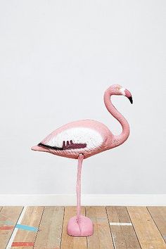 a pink flamingo standing on top of a wooden floor next to a white wall