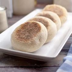 four biscuits on a white plate next to a glass of milk and a napkin in the background