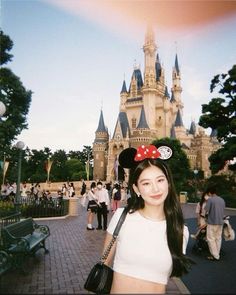 a woman standing in front of a castle with a minnie mouse ears on her head