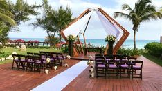 an outdoor ceremony set up with purple chairs and white draping on the beach