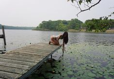 a woman leaning over the end of a dock in water with lily pads on it