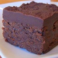 a square piece of chocolate cake on a white plate with a shot glass next to it