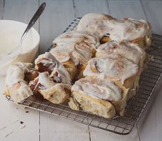 cinnamon rolls with icing on a cooling rack next to a bowl of cream cheese