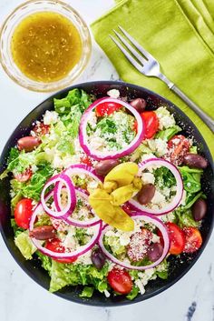 a salad with onions, tomatoes and olives in a bowl next to a fork