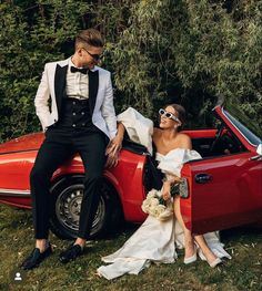 a bride and groom sitting in the back of a red car