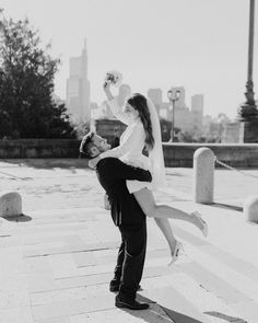 black and white photograph of a bride carrying her groom on his back in front of the city skyline