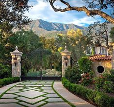 an entrance to a home surrounded by lush green trees and shrubbery with mountains in the background