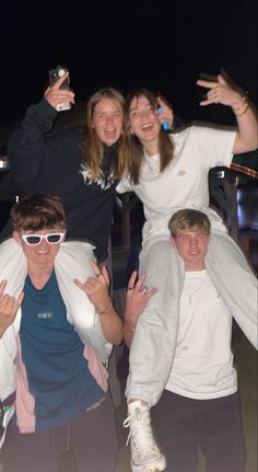 four people are posing for the camera with their arms in the air and one person is wearing sunglasses