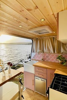 a kitchen area with sink, stove and window looking out to the ocean on a sunny day