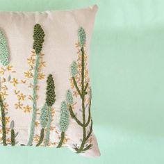 a pillow with crocheted flowers and leaves on the front, against a mint green background