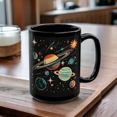 a black coffee mug with an image of the planets on it sitting on a wooden table