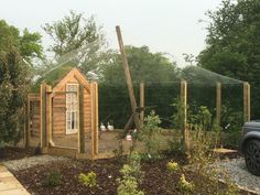 a chicken coop in the middle of a garden with a car parked next to it