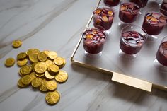 there are many glasses with drinks and gold coins on the table next to each other