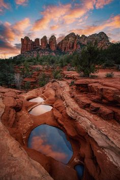 the sun is setting over red rocks and water in a hole that looks like it's going to fall