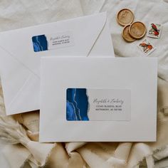 two white envelopes with blue and silver foil on them, next to some coins