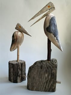 two pelicans sitting on top of wooden stumps with long beaks sticking out of them