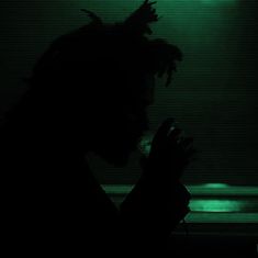 a man with dreadlocks standing in front of a dark background holding his hands together