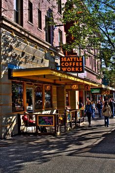 people are walking down the street in front of some shops and stores on a sunny day