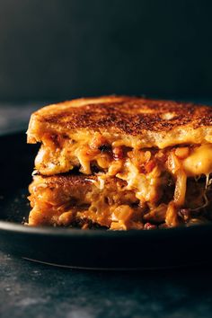 a grilled cheese sandwich on a black plate with melted cheese and chili toppings