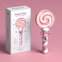 a pink and white candy lollipop next to a box on a pink background