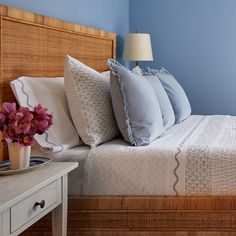 a bedroom with blue walls and white bedding has flowers in a vase on the nightstand