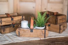 three wooden boxes with plants and candles in them on top of a white cloth covered table