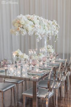 a long table is set with candles and flowers in vases on the side, along with silver chairs