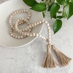 a wooden beaded necklace with tassels on a white plate next to green leaves