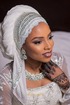 a woman in a white dress and head scarf with jewelry on her hands, posing for the camera