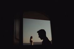 a man and woman standing in the dark looking out an open window at each other