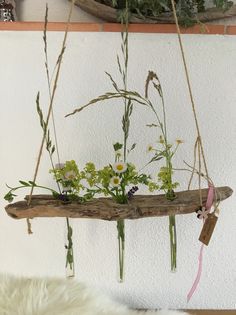 a planter with flowers hanging from it's sides on a wooden beam in front of a white wall