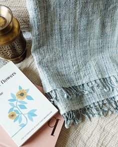 an open book sitting on top of a bed next to a lamp and a blanket