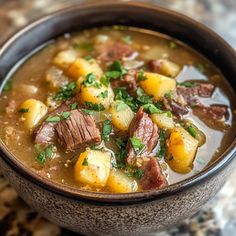 a close up of a bowl of soup with meat and potatoes in it on a table