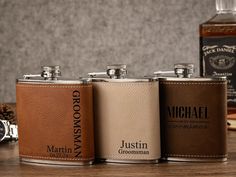 three personalized flasks are lined up on a table next to a watch