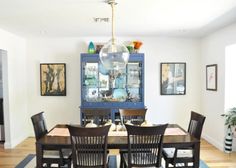 a dinning room table and chairs in front of a blue china cabinet with pictures on the wall