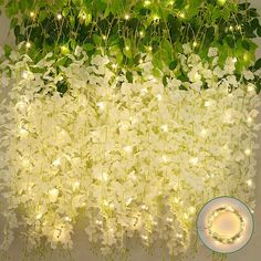 white flowers and green leaves are hanging from the ceiling with fairy lights on them, next to a plate