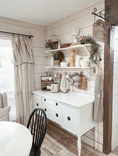 a dining room with white walls and wooden floors is pictured in this image, there are shelves on either side of the table