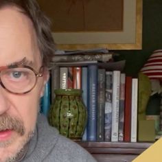 a man with glasses and a beard in front of a book shelf filled with books