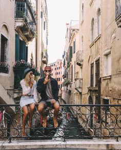 a man and woman sitting on a railing in an alleyway talking on their cell phones