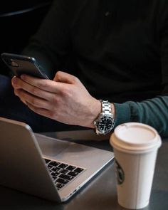 a person sitting at a table with a laptop, cell phone and coffee cup in front of them