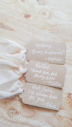 three tags with writing on them sitting on top of a wooden table next to a white cloth