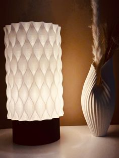 a white vase sitting on top of a table next to a light that is turned on