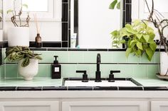 a white sink sitting under a bathroom mirror next to a green tiled counter top with potted plants on it