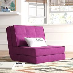 a purple chair sitting on top of a rug in front of a window with a white pillow