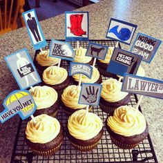 cupcakes with yellow frosting and blue signs are on a black wire rack