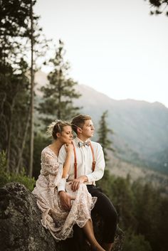 a man and woman sitting on top of a rock